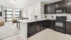 A modern kitchen with dark cabinetry, a central island, and a built-in oven. - DC Charm in Crystal Apartments (Arlington)