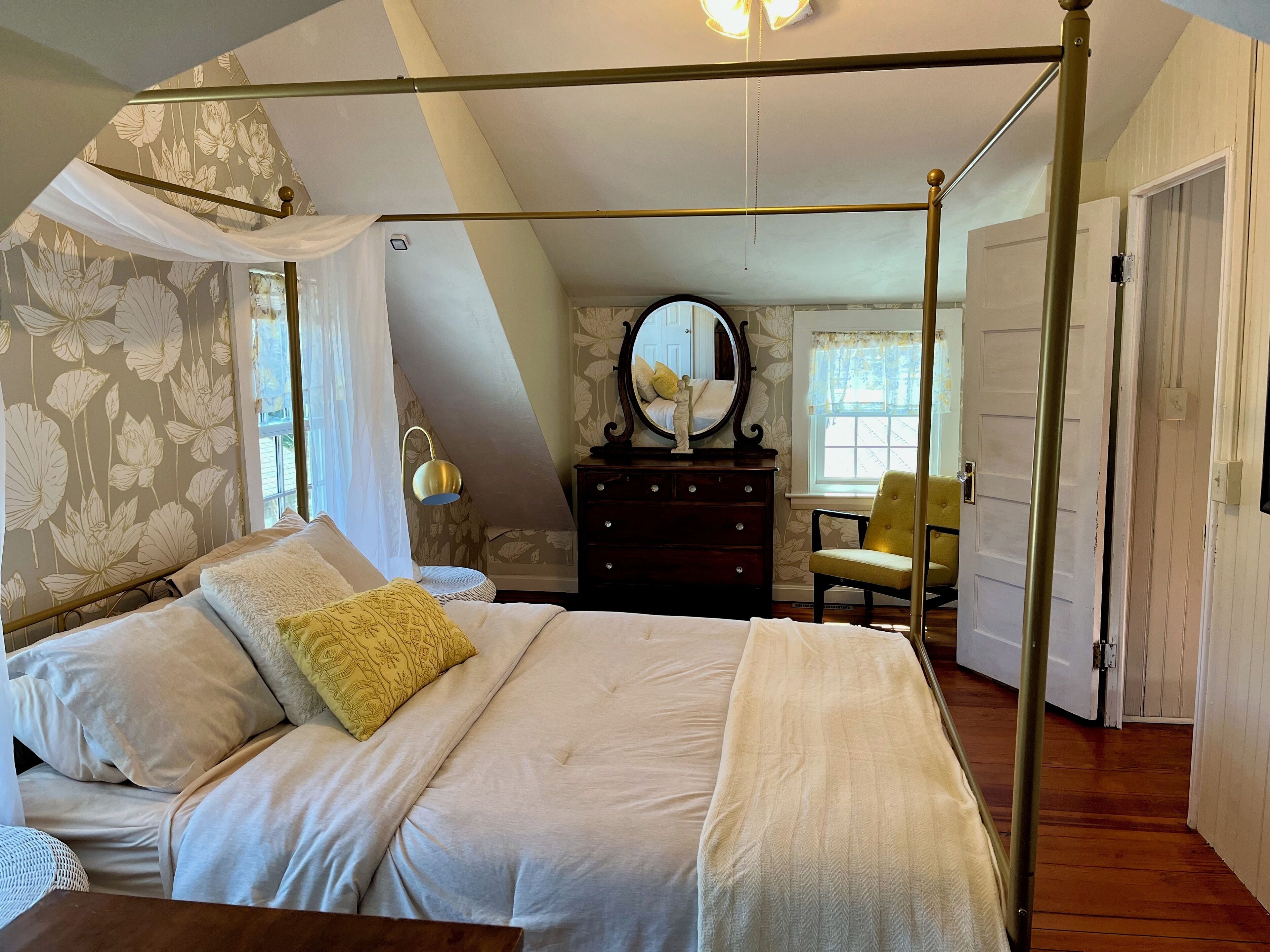 A bedroom with a four-poster bed, a dresser, a chair, and a mirror.