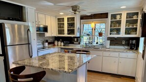 A modern kitchen with white cabinetry, a granite island, stainless steel appliances, and a window with a view.