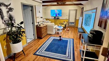 A spacious living area with wooden flooring, a blue rug, a television, and a dining table with chairs.