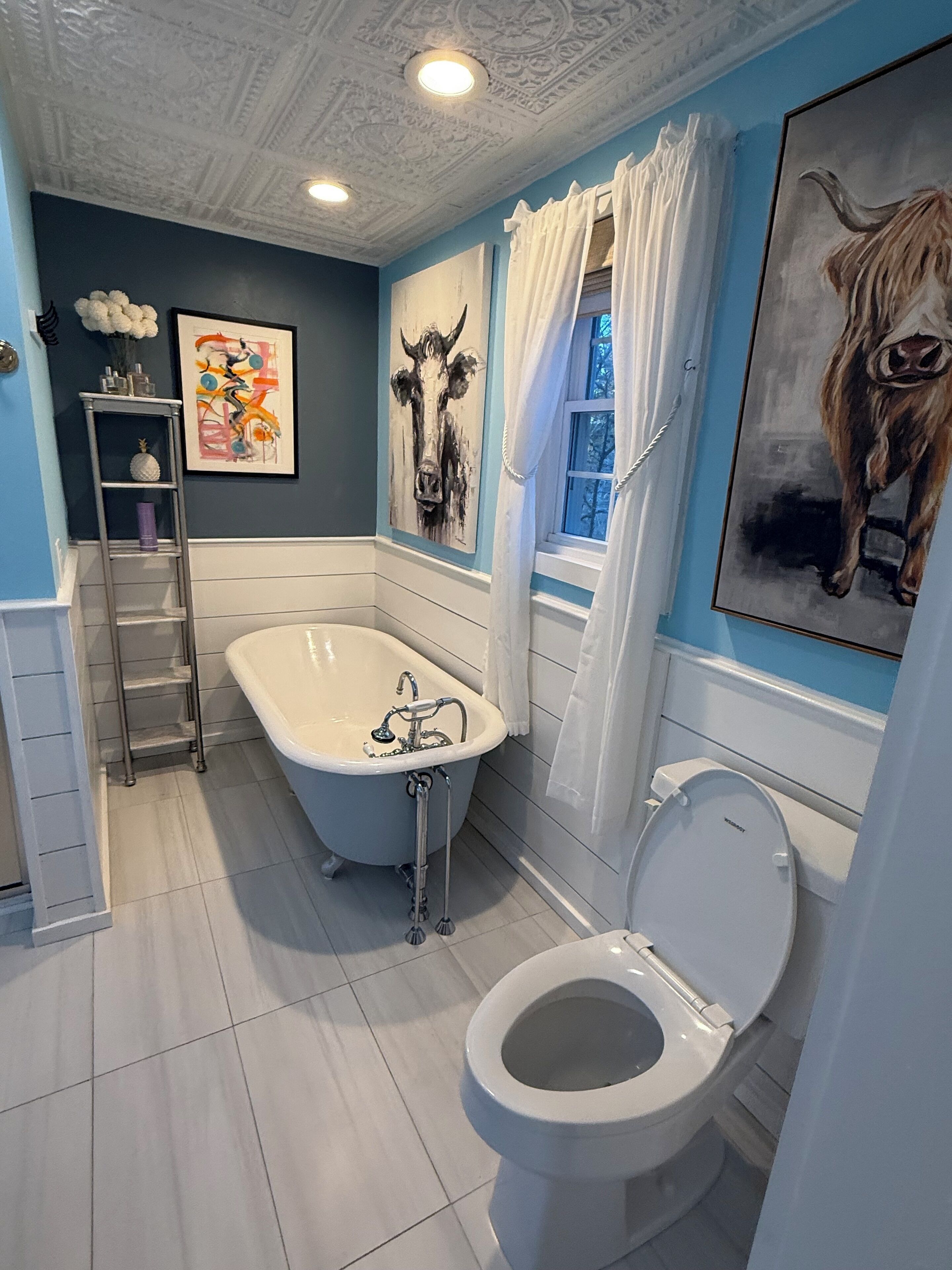 A bathroom with a freestanding bathtub, a toilet, and a window with curtains.
