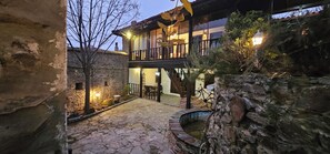 Un patio de piedra con un banco de madera, una pequeña fuente y un edificio con balcón.