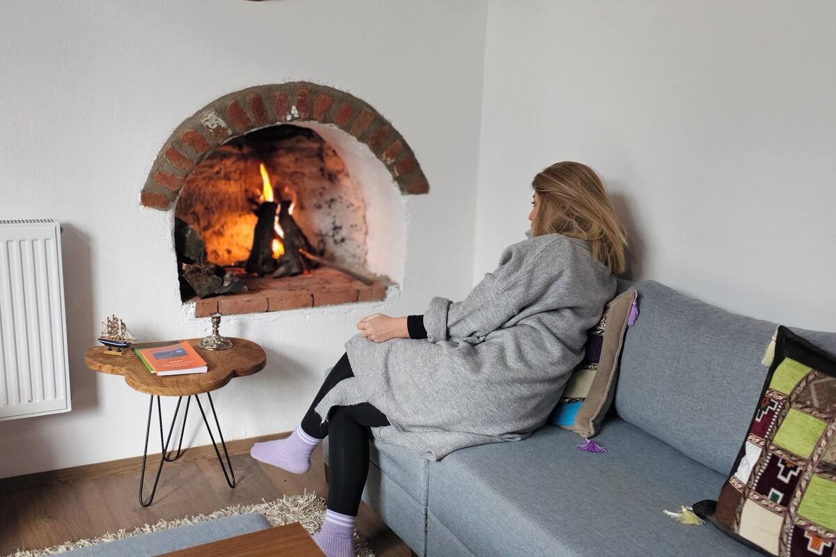 Ein Zimmer mit Kamin aus Backsteinen, einem grauen Sofa, einem kleinen Holztisch mit einem Buch und einem Dekorationsgegenstand sowie einer Heizung.