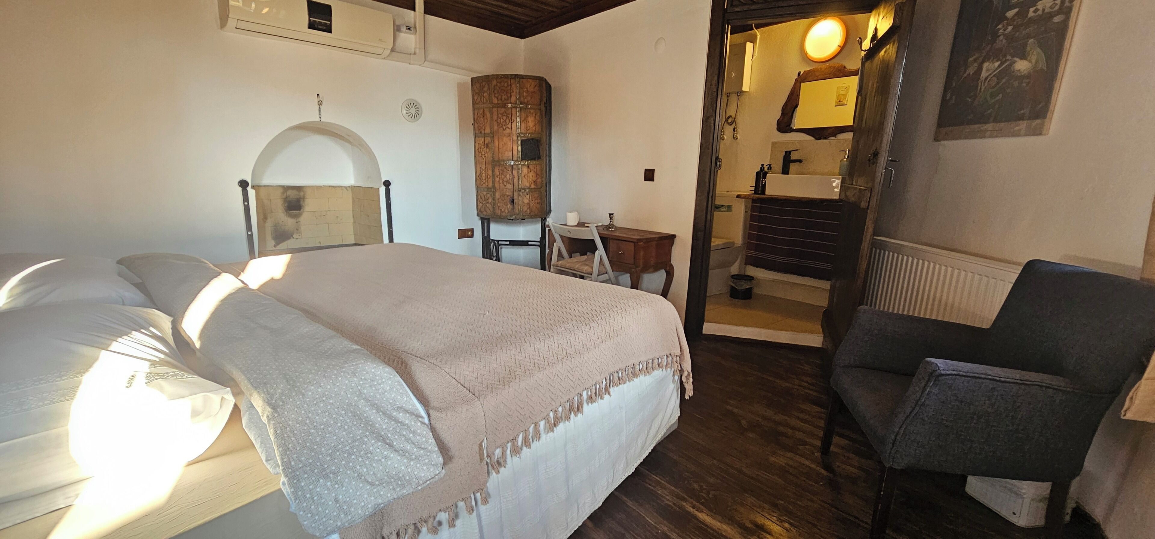 A bedroom with a bed, a chair, a small table, and a bathroom visible through an open door.