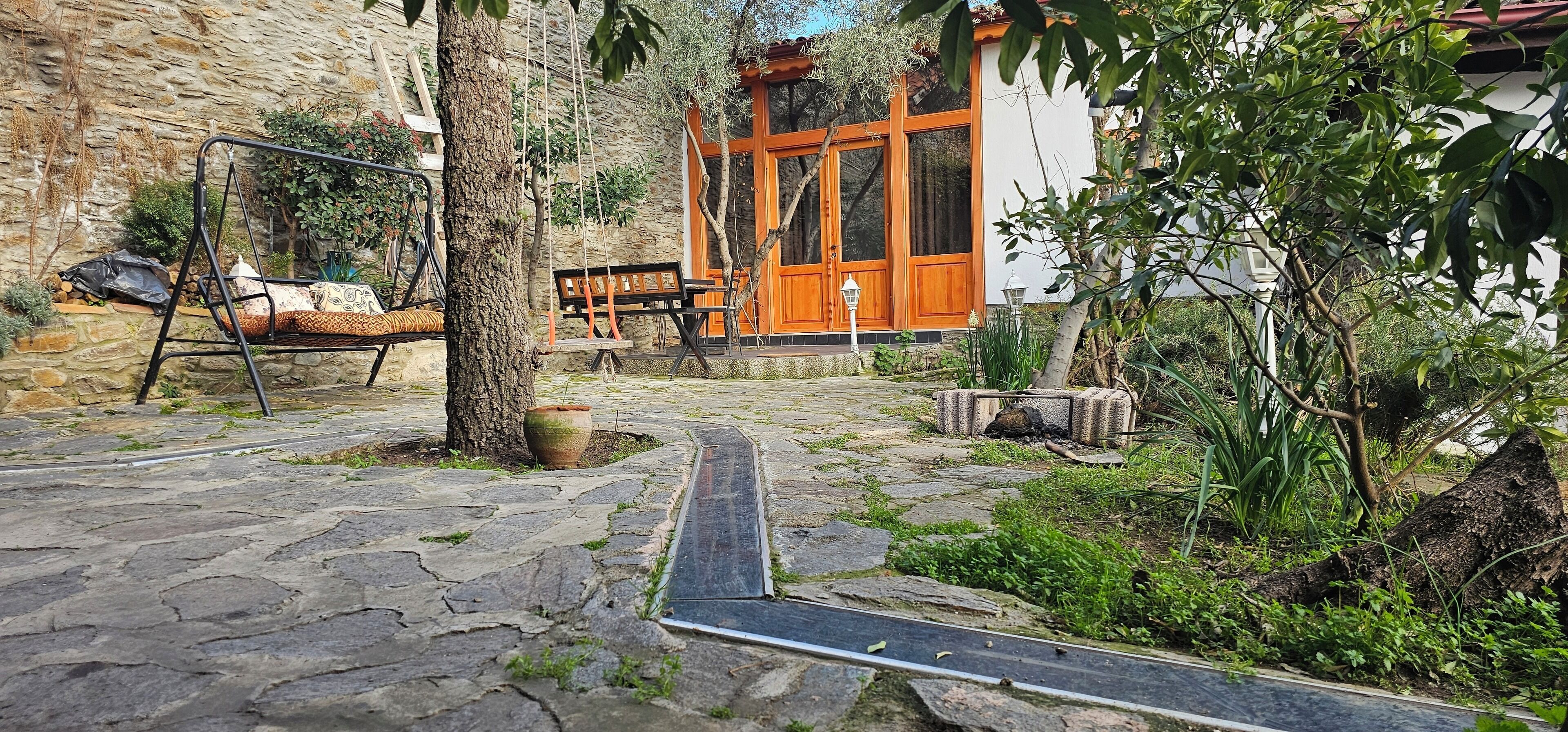 A stone-paved courtyard with a swing set, a bench, and a wooden door.