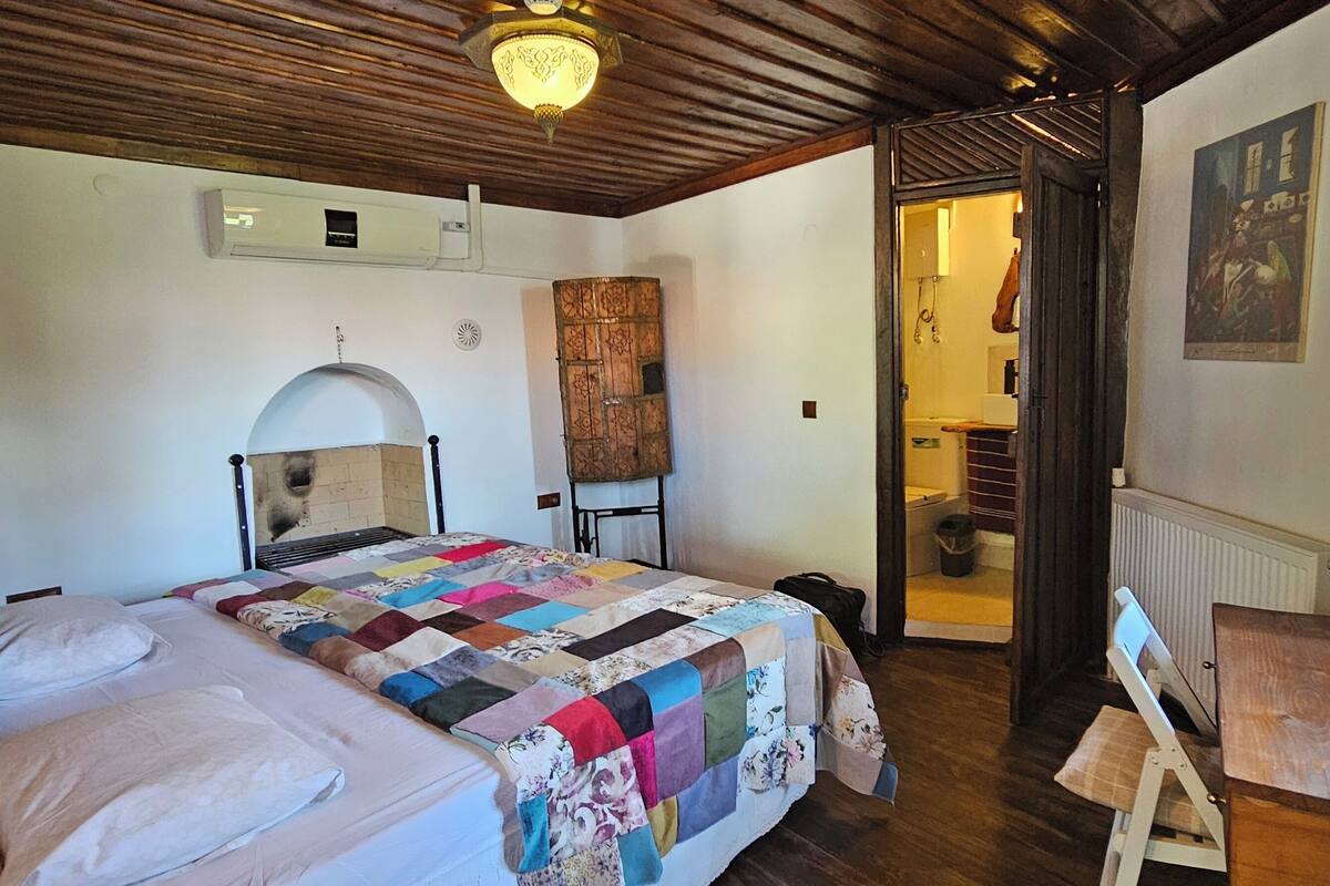 Ein Schlafzimmer mit einem großen Bett, einer Holzbalkendecke, einer Wand-Klimaanlage und einer Tür zu einem Badezimmer.