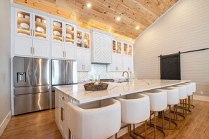A modern kitchen with white cabinetry, stainless steel appliances, and a central island with bar stools. - Timeless Architecture. 6 bedrooms, 8 bathrooms! Sleeps 16! Heart of Three Oaks! (Three Oaks)