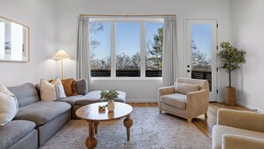 A modern living room with a grey sectional sofa, a round coffee table, a beige armchair, and a large window with curtains. - Amazing Panoramic Views From This Luxury Retreat, Enjoy The Sauna On Top Deck. (Chattanooga)