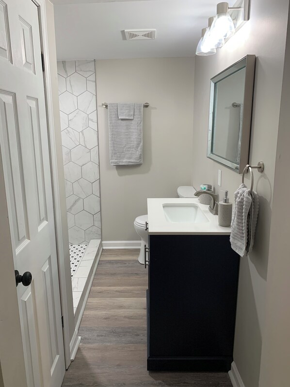 A modern bathroom with a white vanity, a mirror, a toilet, and a shower area.