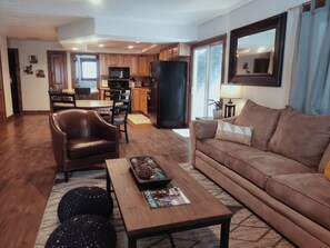 A living room with a brown leather sofa, a coffee table with magazines, and a dining area with wooden chairs and a table.