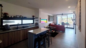 A modern kitchen with a central island, a dining area with a red sofa, and a large window with a view. - Modern 2 bed/2 bath, 1st floor condo. 
Casa Ventosos (Calypso 102). (La Ventana)