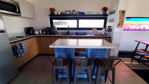 A modern kitchen with a central island, bar stools, a microwave, and a coffee maker. - Modern 2 bed/2 bath, 1st floor condo. 
Casa Ventosos (Calypso 102). (La Ventana)