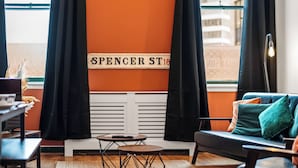 A cozy room with a black sofa, a small round table, and a radiator. A sign on the wall reads "SPENCER ST 18". - The Jewel Box 3BR Apt, JQ Birmingham with Parking (birmingham)