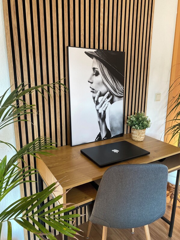A modern workspace with a wooden slat wall, a laptop on a wooden desk, a grey chair, and a small potted plant.
