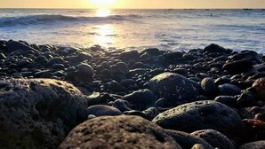 A rocky beach with the sun setting over the ocean.