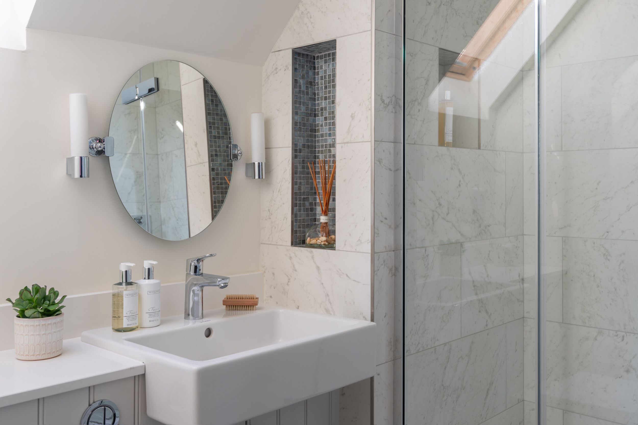 Une salle de bain moderne avec un lavabo blanc, un miroir rond et une cabine de douche en verre.