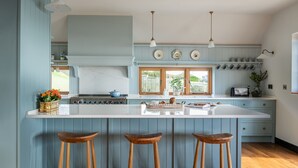 A kitchen with a large island, wooden bar stools, and a window with a view of greenery. - Yellow Sands -  a house that sleeps 10 guests  in 5 bedrooms (Thurlestone)