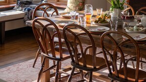 A dining area with wooden chairs, a table set for a meal, and a view of the sea through large windows. - Yellow Sands -  a house that sleeps 10 guests  in 5 bedrooms (Thurlestone)