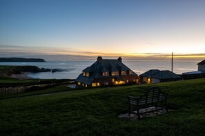 Une maison située sur la côte, avec un toit de chaume, une pelouse verdoyante et un banc.