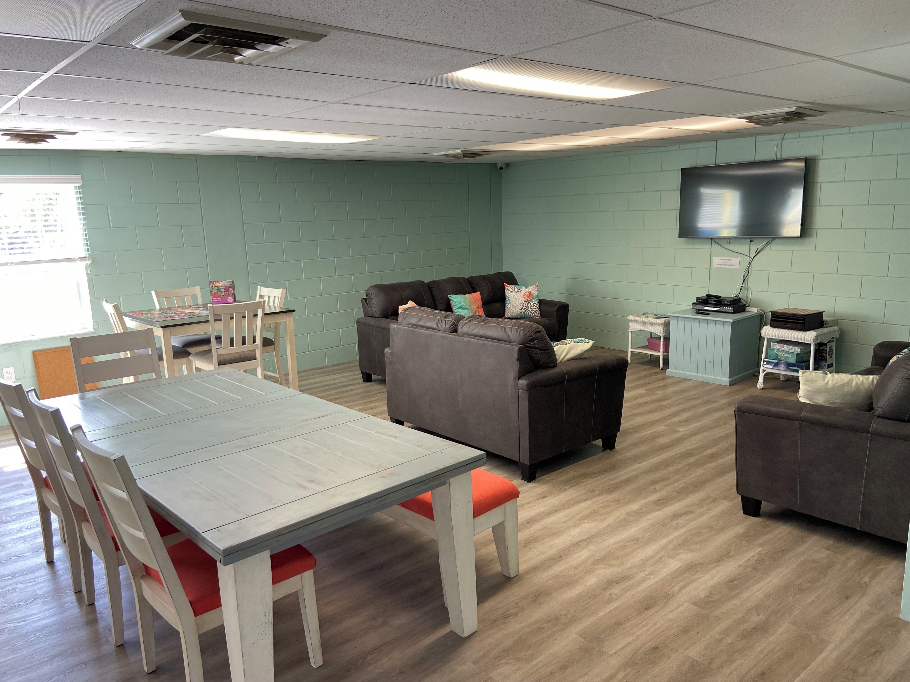 A room with a dining table, two sofas, a TV mounted on the wall, and a small cabinet.