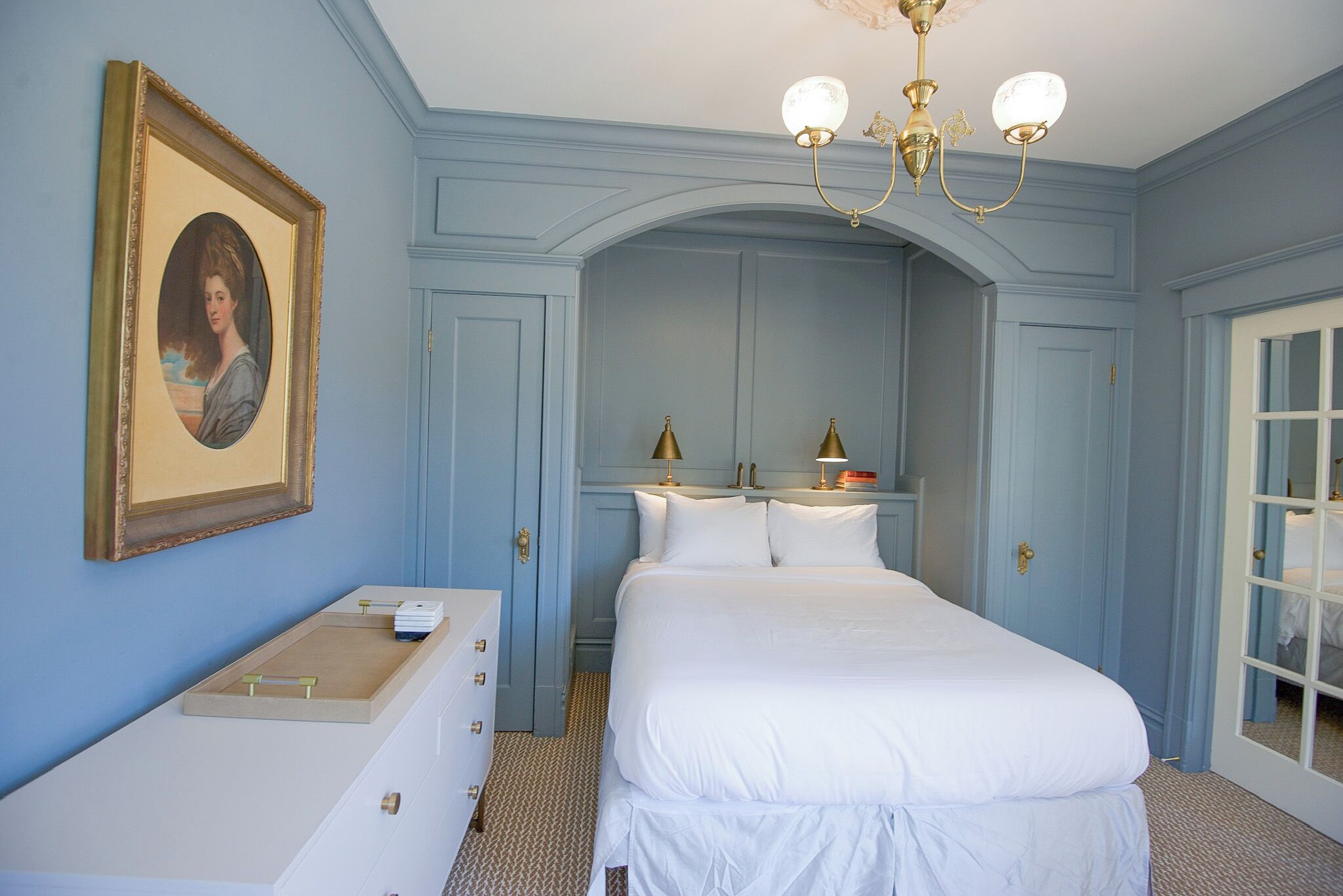 Une chambre à coucher avec un grand lit, une commode, un portrait encadré et un lustre.