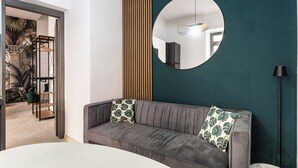 Ein modernes Wohnzimmer mit grauem Sofa, rundem Spiegel und Wand in Grün.