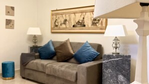 A living room with a grey sofa, blue cushions, a marble side table, and two lit candles on a black surface.