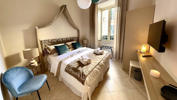 A hotel room with a bed, a chair, a desk with a lamp, a TV, and a window with curtains.