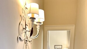 A hallway with a wall-mounted light fixture, a small shelf with a decorative bowl, and a door leading to another room.