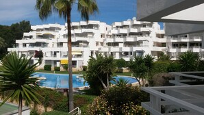 Et moderne hotel med flere balkoner, swimmingpool og frodigt grønt område.