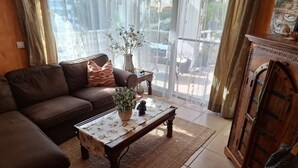 En stue med en brun sofa, et træ sofabord med et blomstret dug, en potteplante og et dekorativt skab.