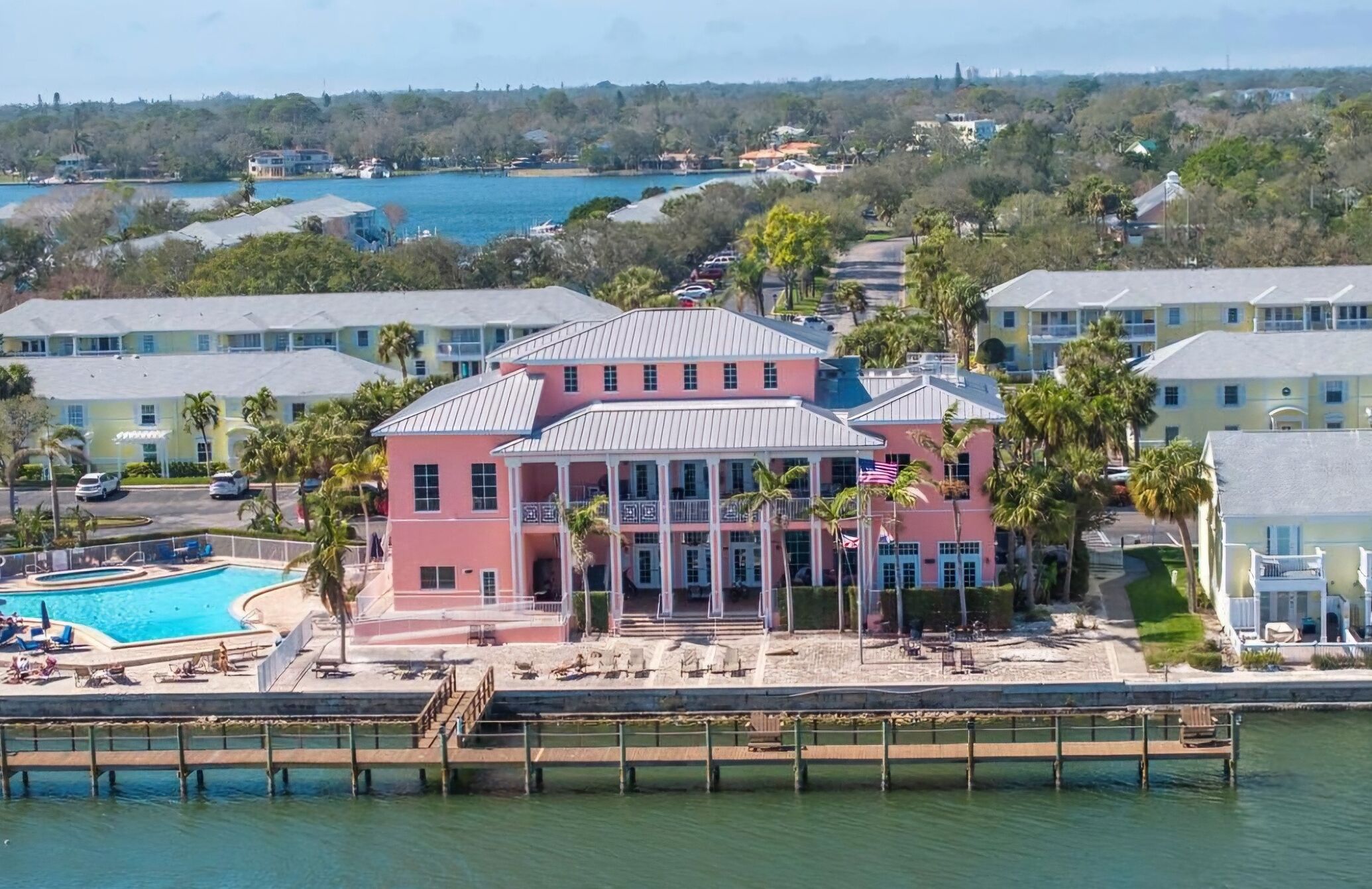 A pink building with a pool, surrounded by palm trees and a dock.