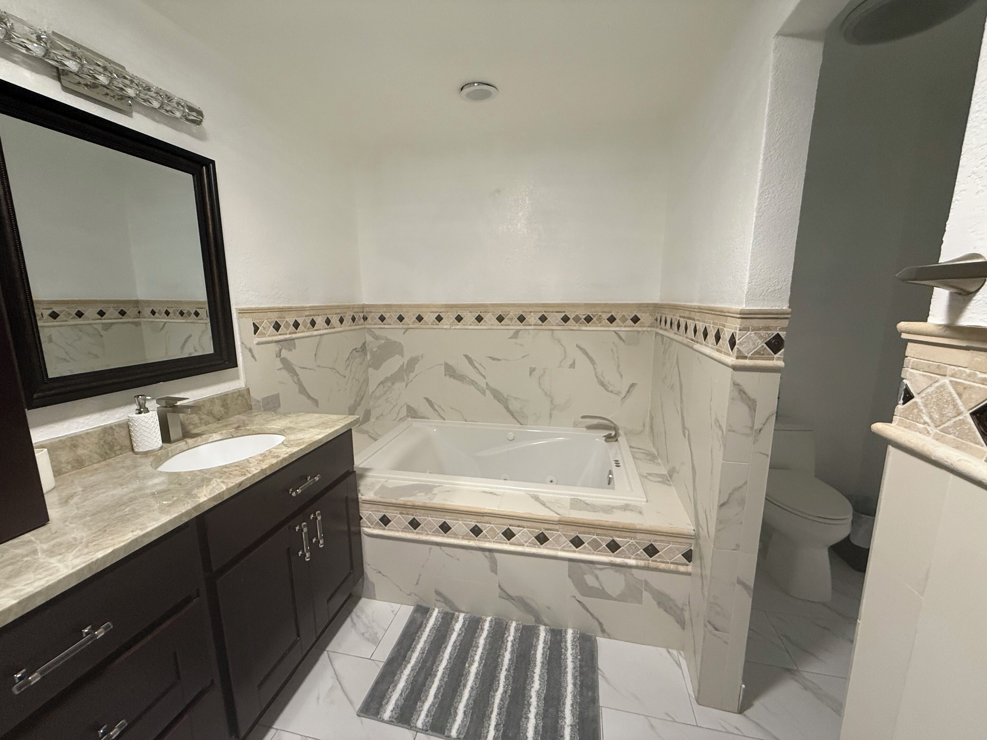 Un baño con lavamanos de mármol, un espejo grande, una bañera y un inodoro.