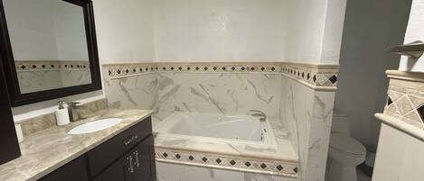 Un baño con lavamanos de mármol, un espejo grande, una bañera y un inodoro.