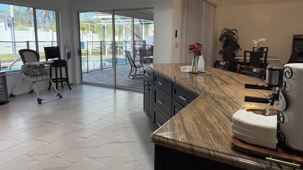 A modern reception area with a marble counter, a seating area with chairs, a large window with a view of a pool, and a ceiling fan. - The Perfect Gateway Home with a large pool area, Gazebo, all fenced in. (Spring Hill)