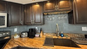 A kitchen with dark wooden cabinets, a granite countertop, a stainless steel sink, and overhead lighting. - The Perfect Gateway Home with a large pool area, Gazebo, all fenced in. (Spring Hill)