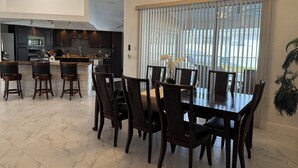 A modern kitchen with dark cabinetry, a central island, and a dining area with a large table and chairs. - The Perfect Gateway Home with a large pool area, Gazebo, all fenced in. (Spring Hill)