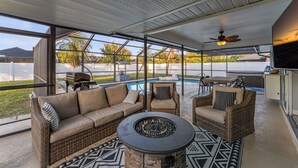 Eine Außenpatio-Terrasse mit Korbmöbeln, einer Feuerstelle und Blick auf einen Swimmingpool.