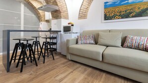 A modern kitchen with a microwave, a dining area with stools, a sofa with patterned cushions, and a large sunflower painting on the wall. - Two steps from theColosseum brand new apartment with maximum comfort for family (Roma)