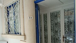 Ein moderner Eingangsbereich mit einem verzierten Metallgitter, einer Nummernschild und einer Tür mit satinierten Glasscheiben.