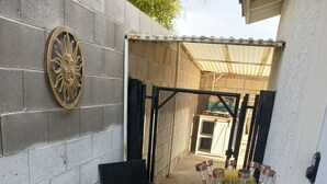A small outdoor seating area with two chairs and a table, a decorative sun emblem on the wall, and a potted cactus.