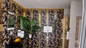 A bathroom with a modern design, featuring a patterned wall, a sink with a gold basin, and a mirror.