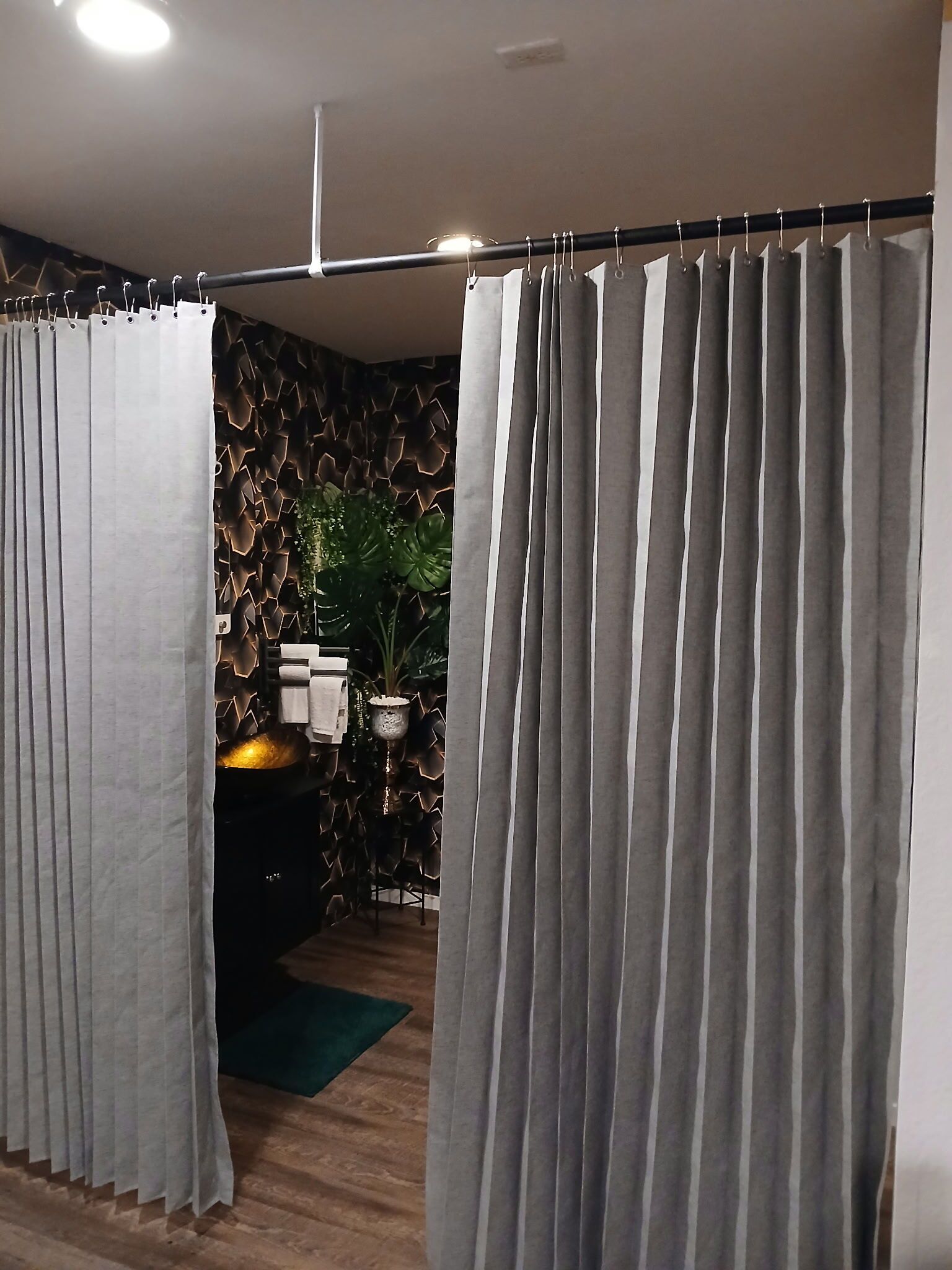 Ein Zimmer mit Vorhangabtrennung, einer Steinwand, einer Pflanze und einem kleinen Tisch mit Gegenständen darauf.
