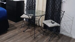A small, modern room with a glass dining table, two chairs, a black TV, a desk, and a blue couch.