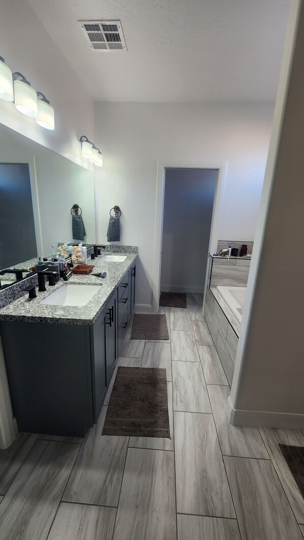 A modern bathroom with a granite countertop, a large mirror, and a walk-in shower. - Lake Powell, Grand Circle, 3-bedroom house with AC, WiFi in welcoming Big Water (Big Water)