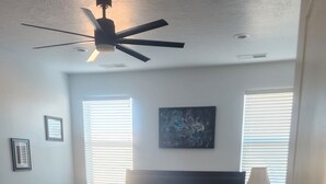 A bedroom with a bed, a ceiling fan, two bedside tables, a nightstand, a lamp, and a window with blinds. - Lake Powell, Grand Circle, 3-bedroom house with AC, WiFi in welcoming Big Water (Big Water)