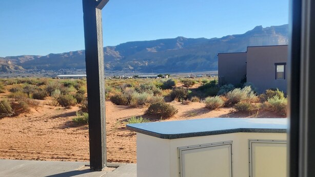 A covered outdoor area with a concrete floor, a white cabinet, and a view of a desert landscape with mountains in the background. - Lake Powell, Grand Circle, 3-bedroom house with AC, WiFi in welcoming Big Water (Big Water)