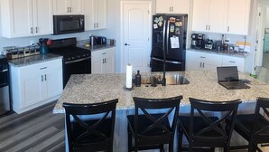 A modern kitchen with white cabinets, a black refrigerator, and a granite countertop. - Lake Powell, Grand Circle, 3-bedroom house with AC, WiFi in welcoming Big Water (Big Water)