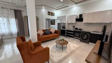 A modern living room with a sofa, coffee table, and a kitchen area with appliances.