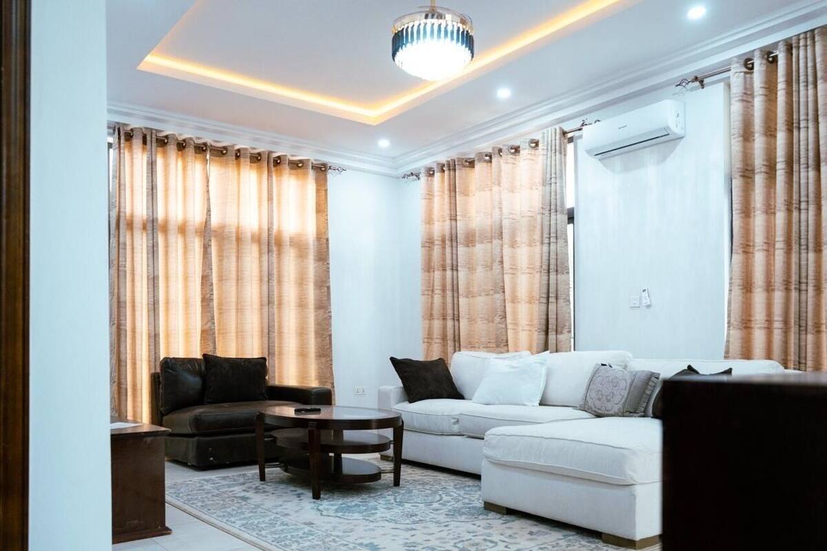 Un salon avec un canapé blanc, un canapé noir, une table basse et un tapis à motifs.